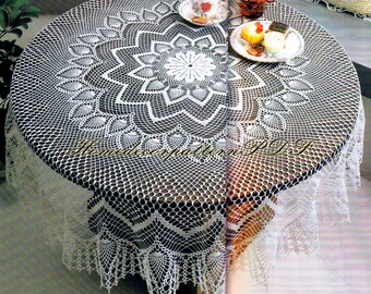 May include: White crocheted tablecloth with a delicate lace pattern and a scalloped edge. The tablecloth is laid over a wooden table with a round top.