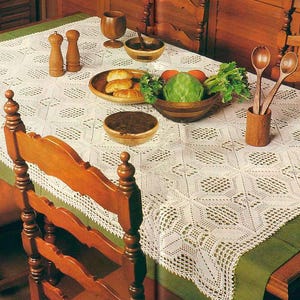 May include: A white rectangular crochet tablecloth with a repeating geometric diamond pattern draped over a green table runner. The table is set with wooden bowls, a wooden goblet, two wooden salt and pepper shakers, and wooden spoons.