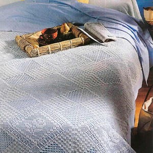 May include: A bed with a light blue bedspread and a yellow pillow. A woven tray holds a cup and saucer, fruit, and a newspaper. The bedspread has a detailed, open weave pattern.