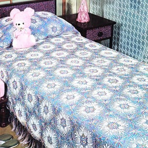 May include: A white crocheted bedspread with a blue and purple pattern and a fringe border. The bedspread is on a bed with a pink teddy bear on the pillow.