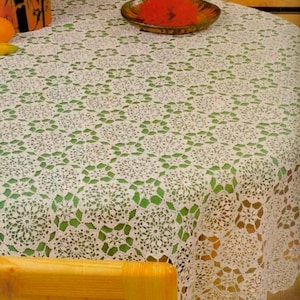 May include: A white, round, crocheted tablecloth with a floral design. The tablecloth is made of a delicate, open-weave fabric, and is draped over a table. The intricate design is visible throughout the cloth.