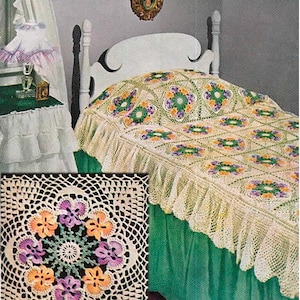 May include: A cream-colored crochet bedspread featuring a repeating square motif with a central floral design in orange, purple, and green. The bedspread has a delicate openwork pattern and a ruffled edge, covering a bed with a white headboard.