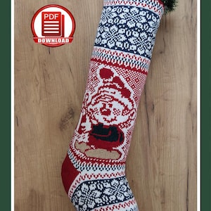 May include: A red, white, and navy blue Christmas stocking with a gnome design. The stocking features a knitted pattern with snowflakes and a gnome wearing a hat. The top is trimmed with green faux pine needles and pine cones.