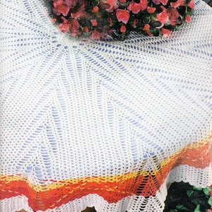 Può includere: Una tovaglia bianca all'uncinetto con bordo smerlato. La tovaglia presenta un design traforato dettagliato che si irradia dal centro. Il bordo presenta fasce arancioni, gialle e rosse. Un bouquet di rose rosa poggia sulla tovaglia.