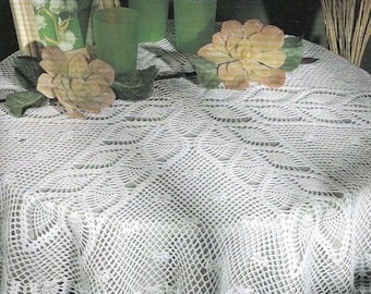 May include: White crocheted table cloth with a delicate lace pattern. The tablecloth is laid on a table with a green background and features a floral design in the center.