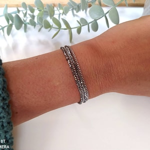 Puede incluir: Un brazalete plateado con múltiples eslabones de cadena. El brazalete está en capas y tiene un diseño delicado y minimalista.