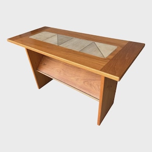 May include: A rectangular wooden side table featuring a warm brown wood grain finish and a central inlay of three light beige ceramic tiles. The table has a solid wood frame with angled side supports and a lower shelf for storage.