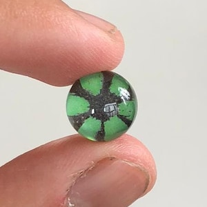 May include: A green glass marble with a black and white design in the centre. The design resembles a flower with six petals.