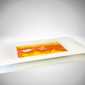 Puede incluir: Una bandeja rectangular de servir de vidrio blanco con una pieza rectangular más pequeña de vidrio con vetas naranja y amarillo en su interior.