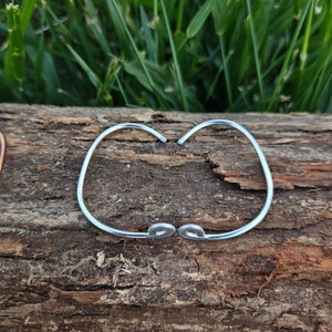 May include: A silver bangle bracelet with a simple, curved design. The bracelet is made of thin metal and has a smooth finish.