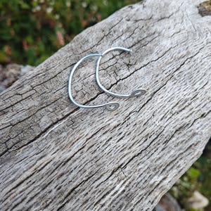May include: A pair of silver-toned metal hoop earrings featuring a thin, curved wire design. Each earring has a small, circular loop at one end and a simple, open-ended construction, showcasing a smooth, polished finish on the metallic surface.
