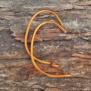 May include: Two orange metal hoops, one slightly larger than the other, are stacked on top of each other. The hoops are lying on a piece of brown wood.