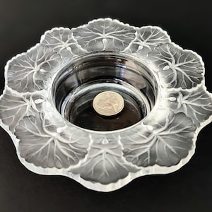 May include: A clear glass dish with a raised design of leaves around the edge. The dish has a smaller, circular inner bowl.