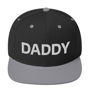 May include: A black and gray baseball cap with a white embroidered word "DADDY" on the front.