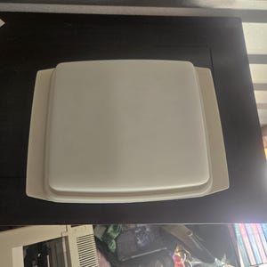 May include: A square, off-white serving tray with a slightly raised rim. The tray sits on a larger, matching rectangular base. The items are on a dark surface.