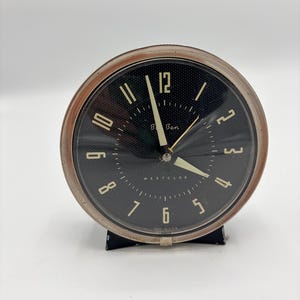 May include: A vintage black and silver Westclox "B Ben" alarm clock. The clock face has white numerals and hands, with the brand name printed in white. The clock is set on a black stand.