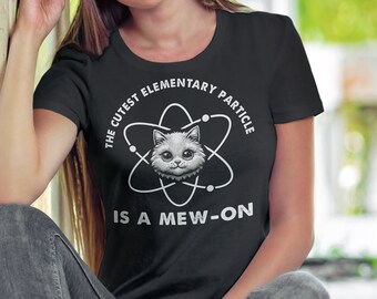 May include: A black t-shirt with a white graphic of a cat inside an atom. The text on the shirt reads "The Cutest Elementary Particle Is A Mew-On."