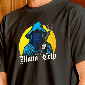 May include: A black t-shirt with a graphic of a hooded figure holding a staff in front of a yellow circle. The text "Mana Grip" is printed below the figure.