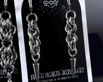 May include: Silver chainmail earrings with a cone-shaped dangle. The earrings are displayed on a black card with the text "BLACK HEARTS JEWELRY HANDMADE & STAINLESS STEEL" and a heart logo.