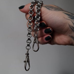 May include: A silver chain with two silver clasps. The chain is made of small, interlocking rings.