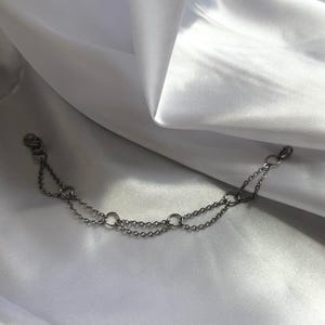 Puede incluir: Un brazalete de cadena de plata con múltiples anillos conectados.