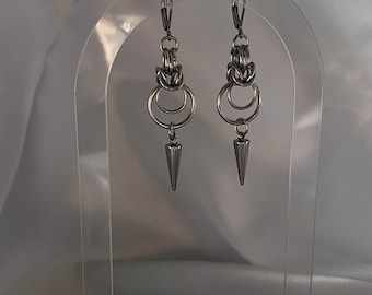 May include: A pair of silver earrings with a geometric design. The earrings feature a series of interlocking rings and a pointed tip.