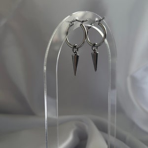 May include: A pair of silver hoop earrings with a pointed silver charm hanging from each hoop.