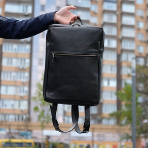 May include: A black leather backpack with a zippered front pocket and adjustable straps.