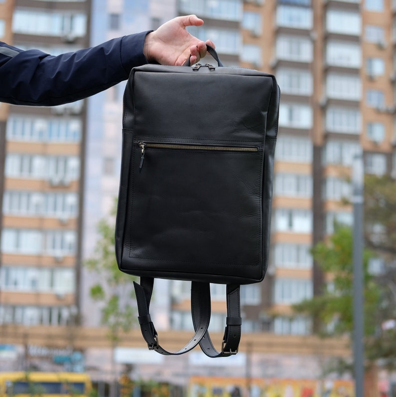May include: A black leather backpack with a zippered front pocket and adjustable straps.