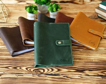Puede incluir: Una colección de diarios de cuero en varios colores, incluyendo marrón oscuro, verde y tostado. El diario verde presenta el nombre Oliver grabado en la cubierta, mientras que el diario tostado presenta el nombre Emily. Cada diario tiene un cierre.