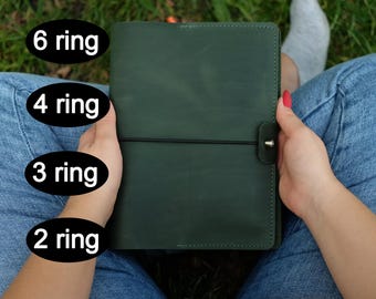 May include: A dark green leather binder featuring a black elastic closure with a metal stud. The image includes text labels indicating options for 6 ring, 4 ring, 3 ring, and 2 ring mechanisms for the planner cover.