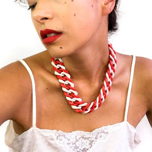 May include: A woman wearing a white tank top with a red and white plastic chain necklace. The necklace is thick and chunky.