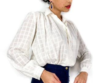 70s/early 80s vintage off-white blouse. Slightly sheer with a discrete checkered print. Tiny bow at the collar. Snap closure.