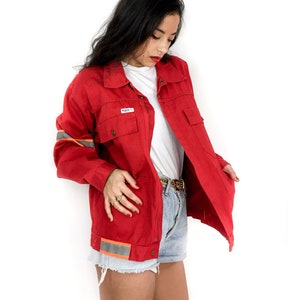 May include: A red work jacket with reflective tape on the sleeves and a white t-shirt underneath. The jacket has a zipper closure and multiple pockets.