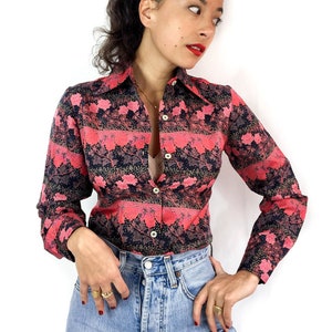 Peut inclure: Une chemise à manches longues à boutons avec un imprimé floral rose et noir. La chemise a un col et une silhouette ajustée.