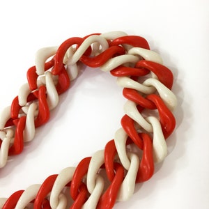May include: A red and white plastic chain necklace. The chain is made of large, chunky links.