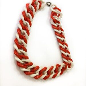 May include: A red and white plastic chain necklace. The necklace is made of large, chunky links that are interlocked.