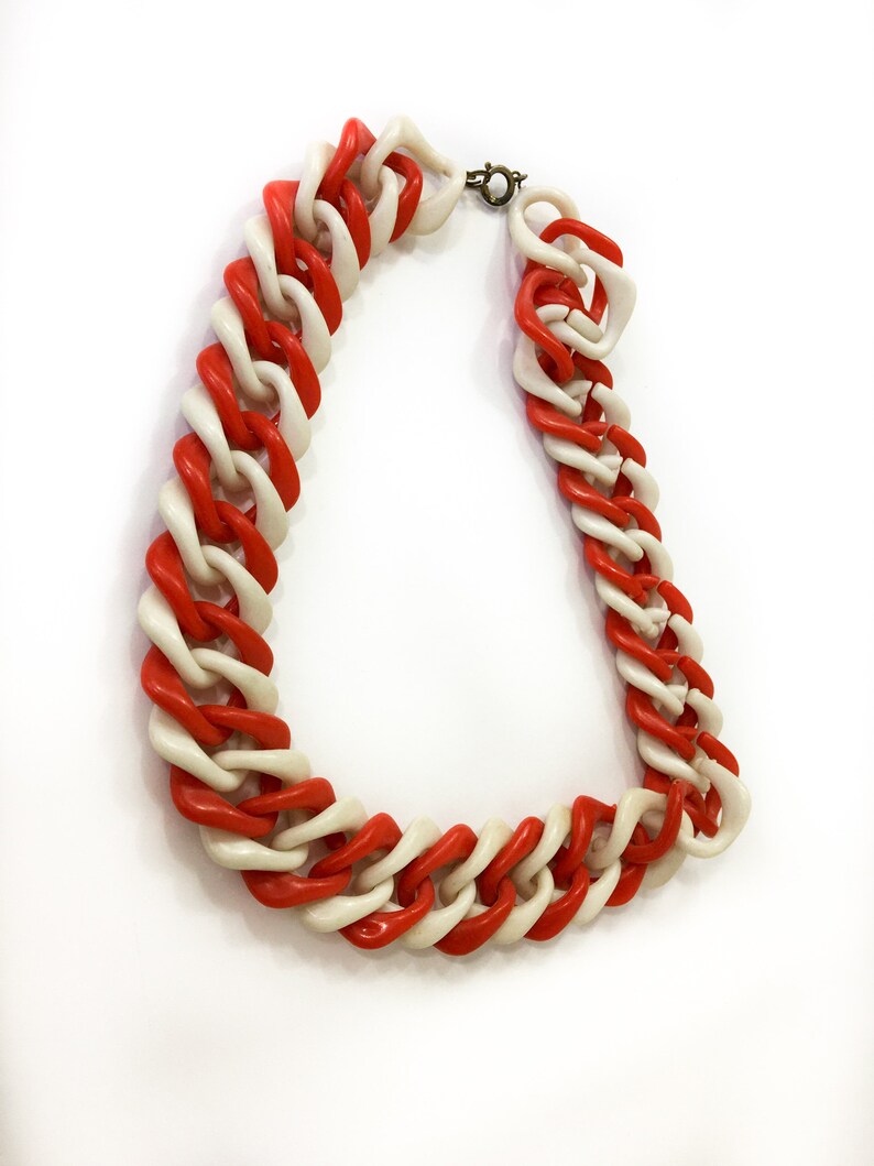 May include: A red and white plastic chain necklace. The necklace is made of large, chunky links that are interlocked.