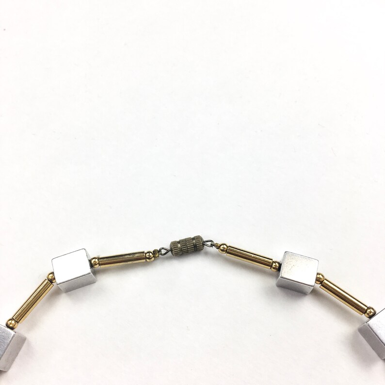 May include: A silver and gold necklace with square-shaped beads and a clasp.