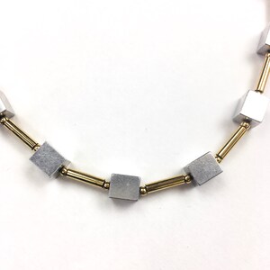 May include: A silver and gold necklace with square-shaped beads. The necklace is made of metal and has a simple design.