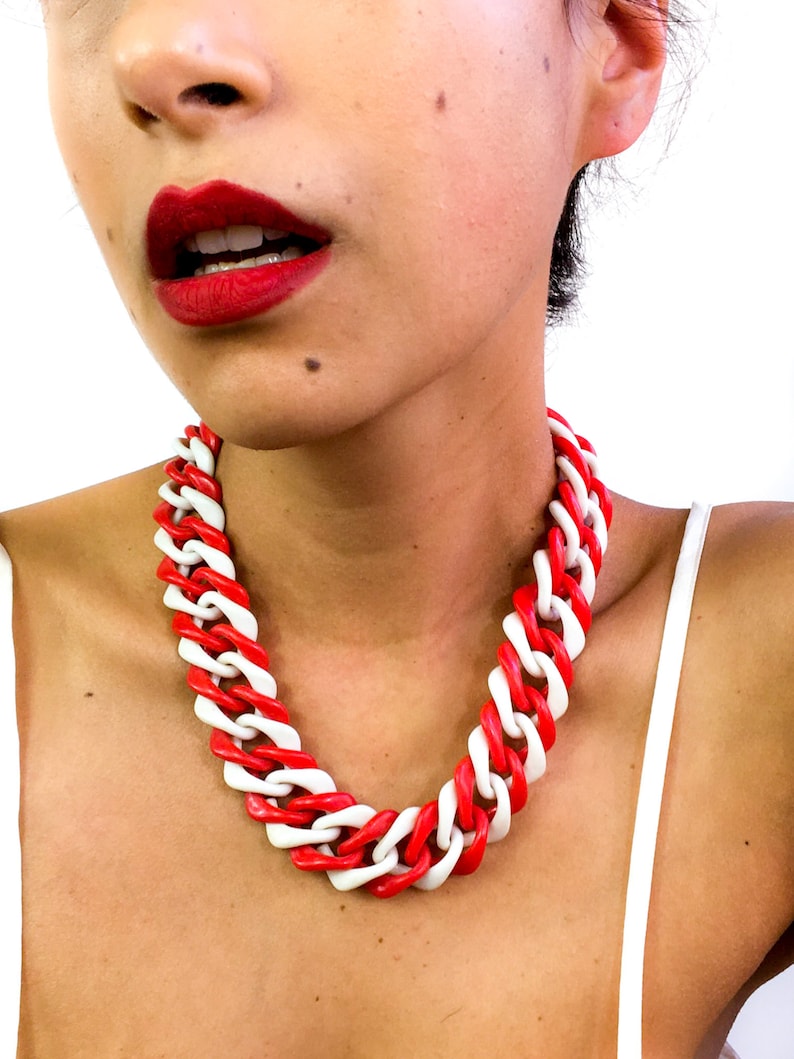 May include: A red and white chunky chain necklace. The necklace is made of plastic and has a bold, geometric design.