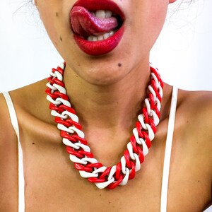 May include: A close-up of a person's mouth with red lipstick and a tongue sticking out. The person is wearing a red and white chunky chain necklace.