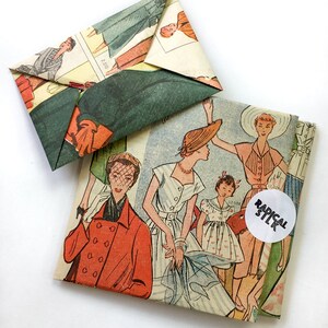 May include: Two vintage paper envelopes with a retro fashion illustration of women wearing dresses and hats. The envelopes are folded and have a white circle sticker with the text "RADICAL STLK" on the larger envelope.