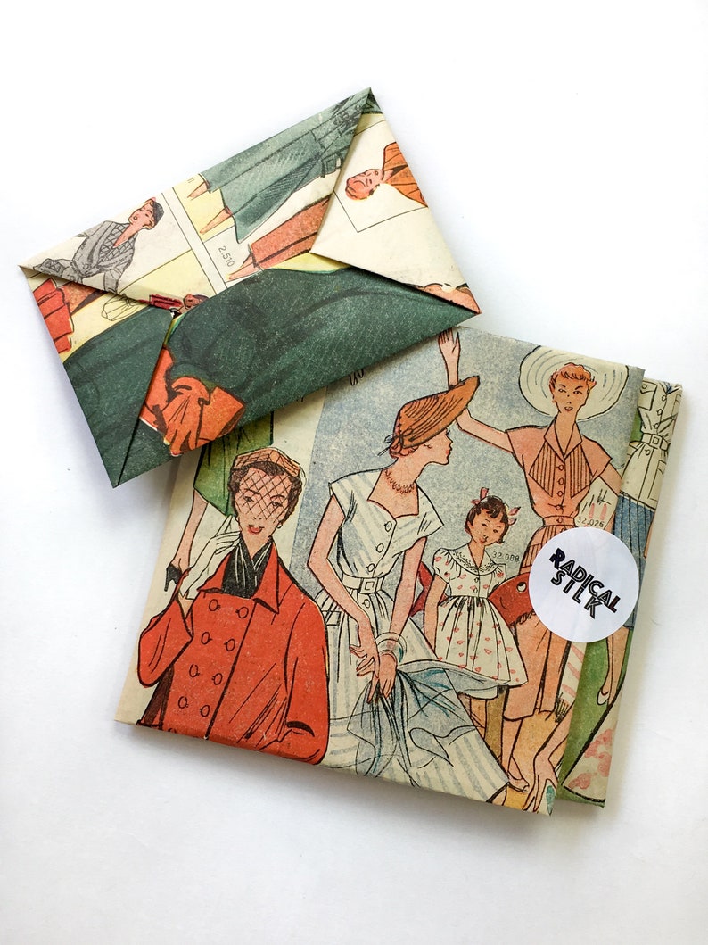 May include: Two vintage paper envelopes with a retro fashion illustration of women wearing dresses and hats. The envelopes are folded and have a white circle sticker with the text "RADICAL STLK" on the larger envelope.