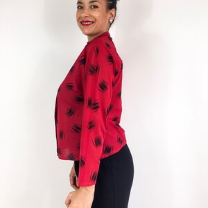 May include: A red long-sleeved blouse with a black abstract print. The blouse has a high neckline and a button-up front.