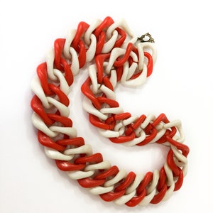 May include: A red and white plastic chain necklace. The chain is made of large, chunky links that are twisted together.