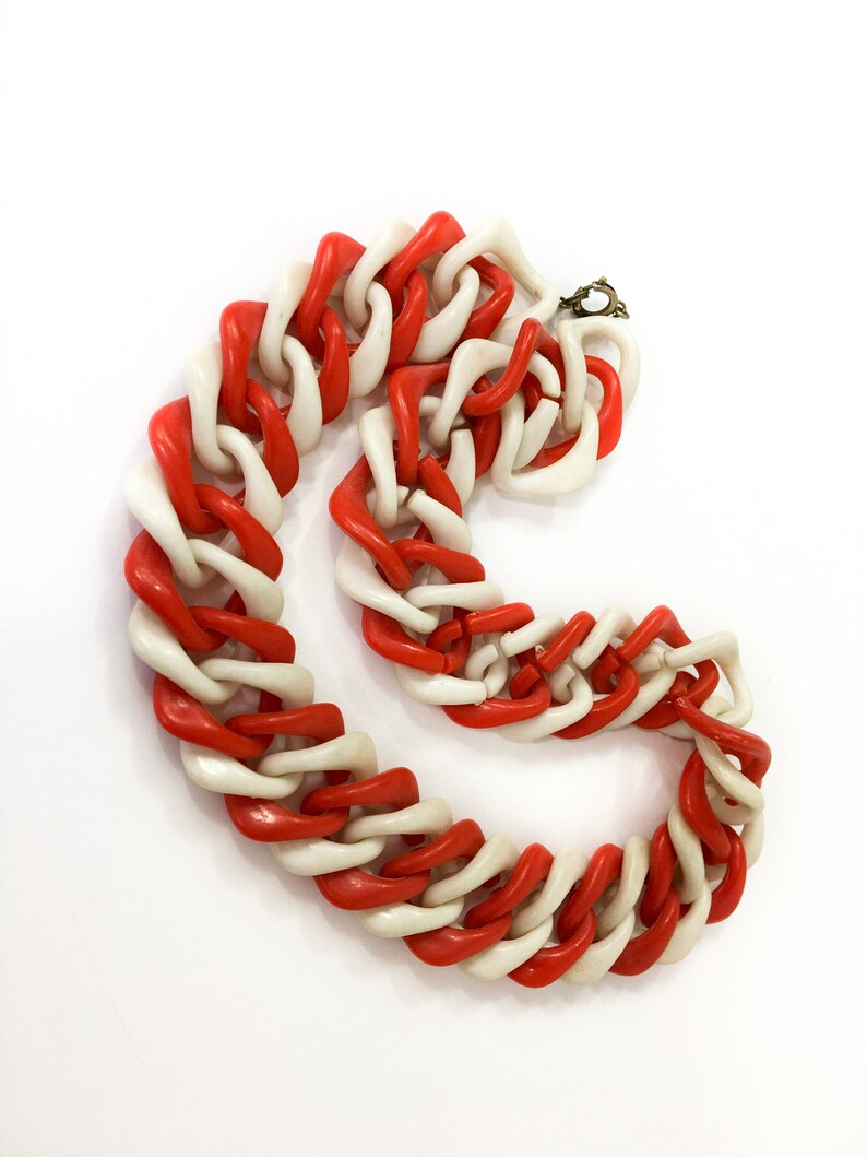 May include: A red and white plastic chain necklace. The chain is made of large, chunky links that are twisted together.