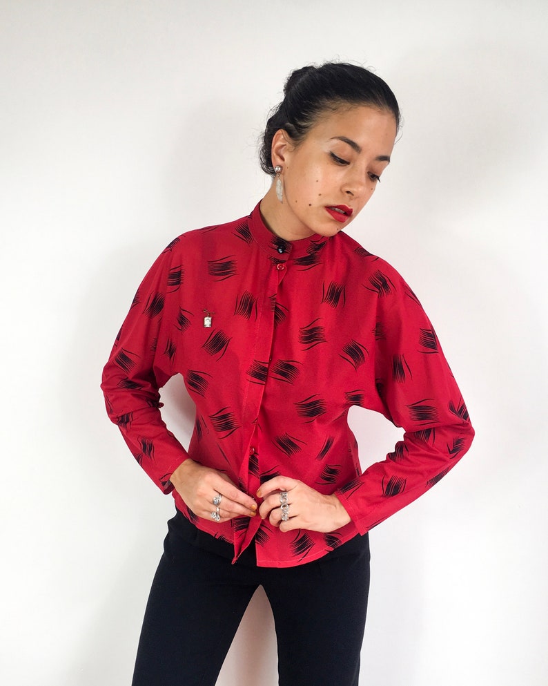 May include: A red long-sleeved button-up shirt with a black abstract print. The shirt has a mandarin collar and a fitted silhouette.