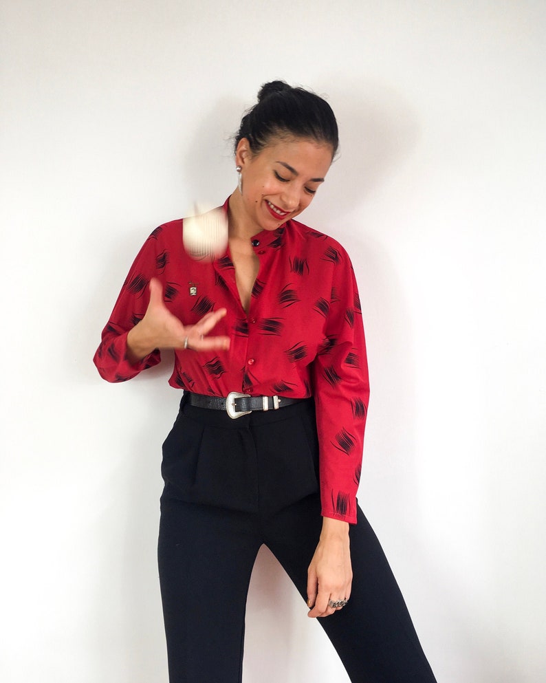 May include: A woman wearing a red and black patterned button-down shirt with black pants and a black belt.