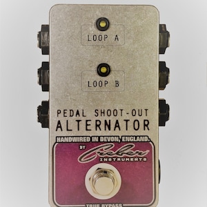 May include: A silver Pedal Shoot-Out Alternator guitar effects pedal with the text "LOOP A" and "LOOP B". The pedal has a purple and white label that reads "Crober Instruments" and "True Bypass".